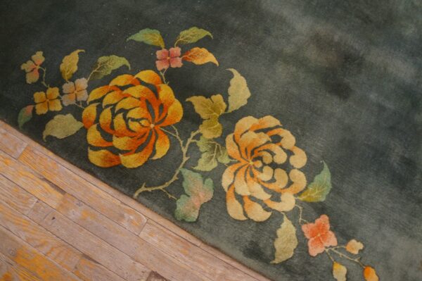 Detail shot of a plush teal rug featuring stylized orange and gold flowers on wood plank flooring.