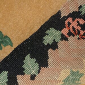 Low-pile tan rug with green shapes, rolled up to show a tight geometric weave resting on wood planks.