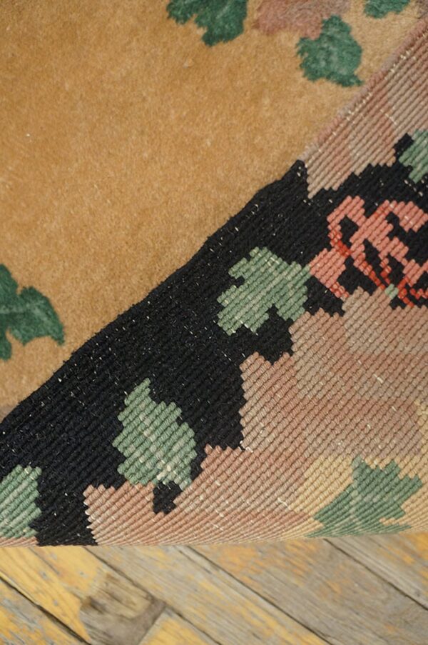 Low-pile tan rug with green shapes, rolled up to show a tight geometric weave resting on wood planks.