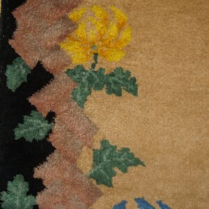 Tan rug detail showing a yellow floral motif and patterned border beside distressed wood flooring.