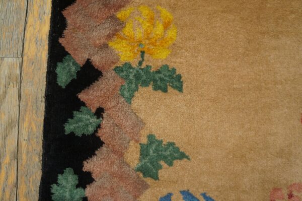 Tan rug detail showing a yellow floral motif and patterned border beside distressed wood flooring.