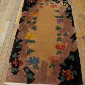 Rectangular runner with a gold field, rust jagged border, black edge, and multicolored floral sprays on a wood floor.