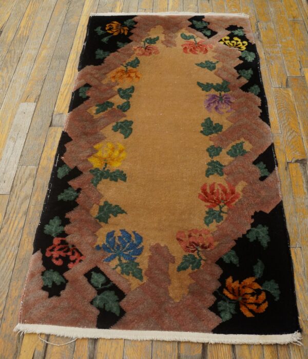 Rectangular runner with a gold field, rust jagged border, black edge, and multicolored floral sprays on a wood floor.