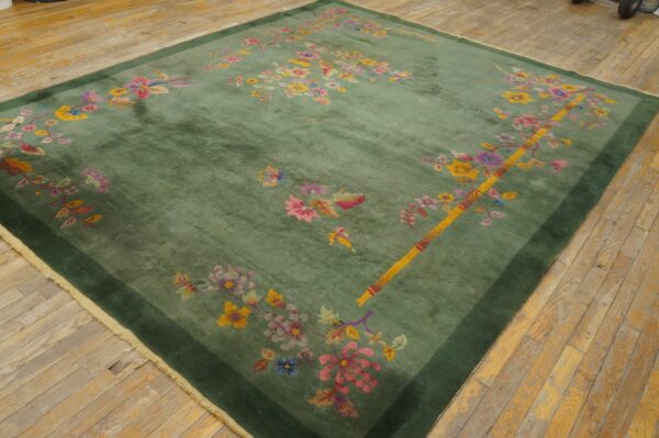 Green pile rug with bright pink and yellow floral patterns and a dark green border on plank flooring.