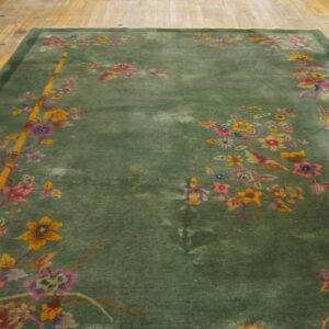 Green rug with multicolored flowers and yellow bamboo accents rests on light wooden plank flooring.
