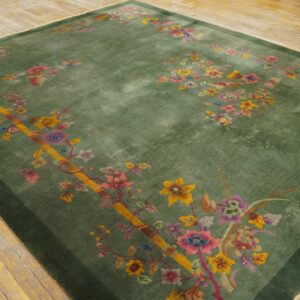 Green rug with bright multicolored floral pattern and dark border rests on a distressed wooden floor.