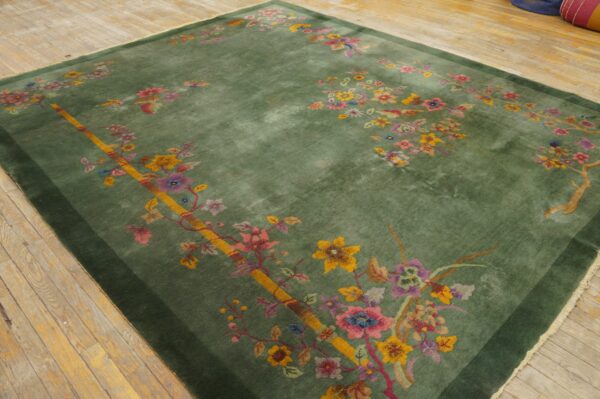Green rug with bright multicolored floral pattern and dark border rests on a distressed wooden floor.