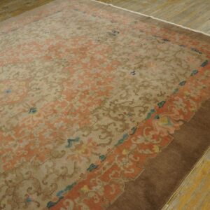 Ornate tan and peach rug with a brown border resting on distressed wood plank flooring.