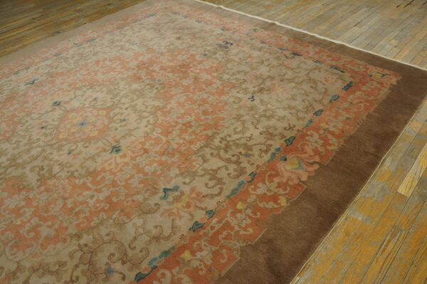 Ornate tan and peach rug with a brown border resting on distressed wood plank flooring.