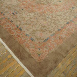 Low pile, tan rug with peach and blue floral patterns, bordered in brown, rests on worn wood planks.