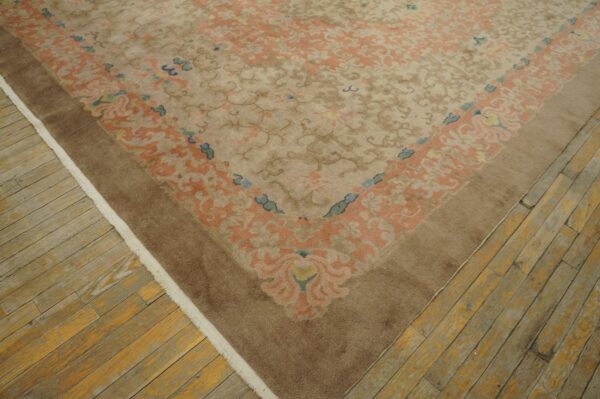 Low pile, tan rug with peach and blue floral patterns, bordered in brown, rests on worn wood planks.