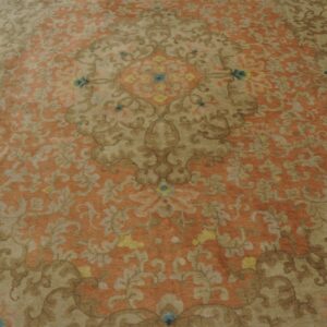 Ornate floral rug pattern in muted rust orange, tan, and brown with small blue and yellow details.