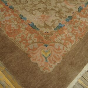 Muted brown rug corner featuring a scrolling floral pattern in peach, tan, blue, and yellow on distressed wood floors.