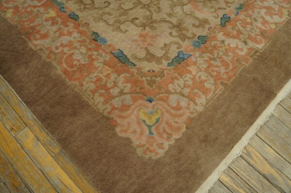 Muted brown rug corner featuring a scrolling floral pattern in peach, tan, blue, and yellow on distressed wood floors.