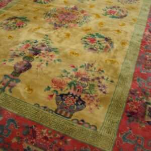 Angled view of a golden high-pile rug with colorful floral motifs and complex red and teal borders on wood floors.