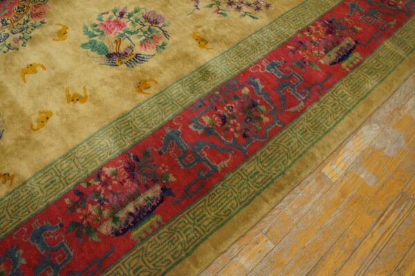 A high-pile gold rug with floral details and a wide red border rests on worn yellow wood flooring.