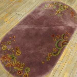 Plum-colored oval rug with colorful floral and grape designs resting on worn light wooden floorboards.