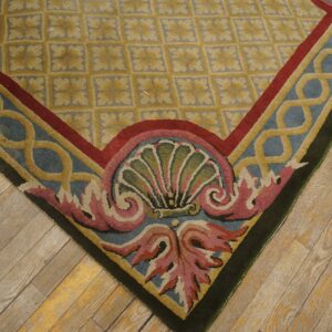 Low-pile rug corner showing gold lattice field and blue border with pink shell scrollwork on wood floors.