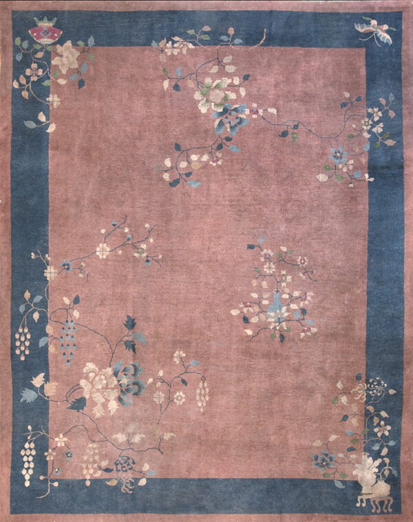 Rose-mauve field rug with a wide blue border featuring large floral vines and various decorative motifs.