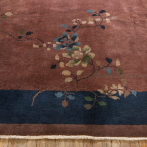 A terracotta rug with scattered floral patterns and a wide navy border rests on wood planks.