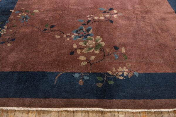 A terracotta rug with scattered floral patterns and a wide navy border rests on wood planks.