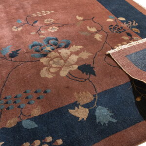 A rusty-red rug with blue and gold floral vines has its deep navy border corner folded up.