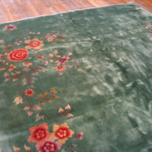 Green high-pile rug with variegated texture and large red, pink, and yellow floral designs on wood flooring.