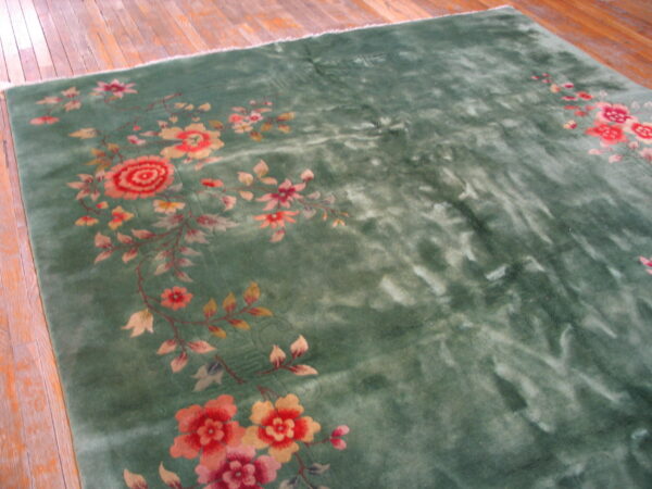 Green high-pile rug with variegated texture and large red, pink, and yellow floral designs on wood flooring.