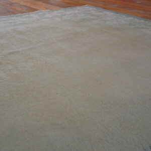 Textured, solid sage-gray rug with visible pile variations rests on a warm wood floor.