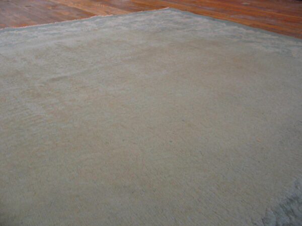 Textured, solid sage-gray rug with visible pile variations rests on a warm wood floor.