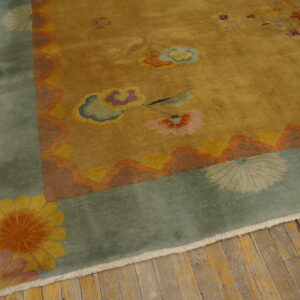 Golden yellow rug with colorful floral motifs, a wide sage border, and fringe rests on plank wood flooring.