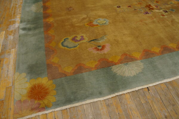 Golden yellow rug with colorful floral motifs, a wide sage border, and fringe rests on plank wood flooring.