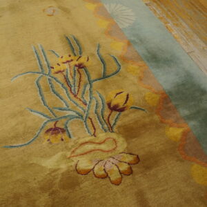 High-pile gold rug with a detailed floral pattern and sage green border on weathered wood planks.