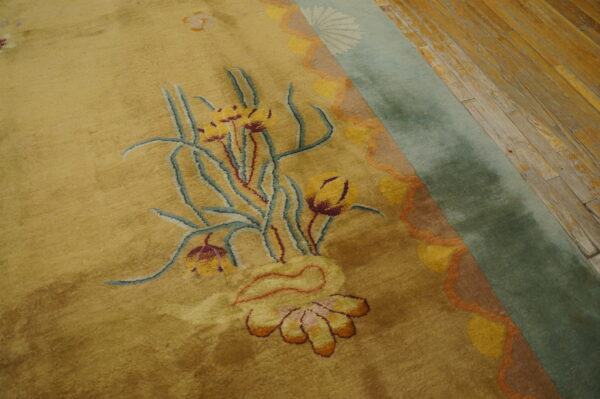 High-pile gold rug with a detailed floral pattern and sage green border on weathered wood planks.
