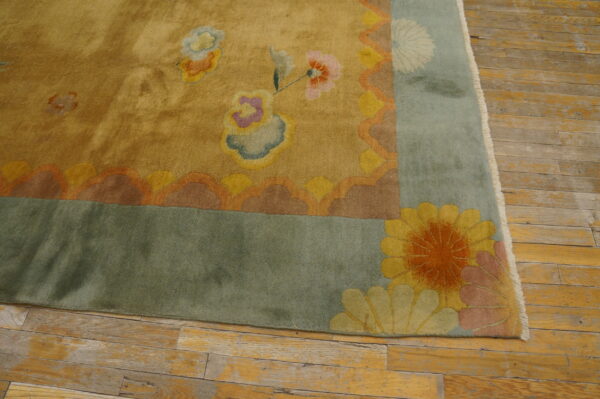 Low pile yellow rug corner with a blue-green border and multicolored floral designs on worn wood flooring.