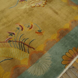 Plush gold and multi-colored rug with complex floral designs and a teal border folded over wood planks.