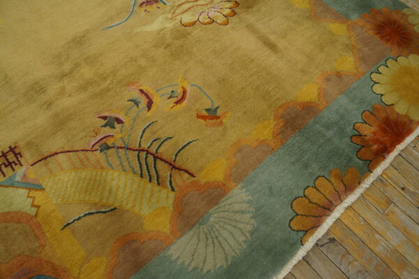 Plush gold and multi-colored rug with complex floral designs and a teal border folded over wood planks.