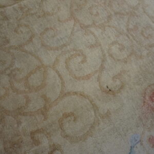 Close-up of a low-pile rug with beige field and muted curvilinear motifs in rust, pink, and light blue.