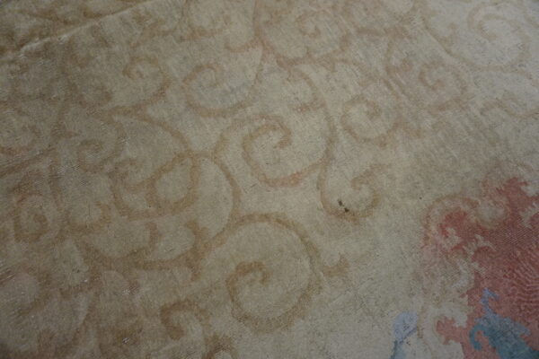 Close-up of a low-pile rug with beige field and muted curvilinear motifs in rust, pink, and light blue.