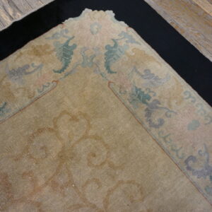 Faded tan rug with pastel floral border sits over a black mat on distressed wood floors.