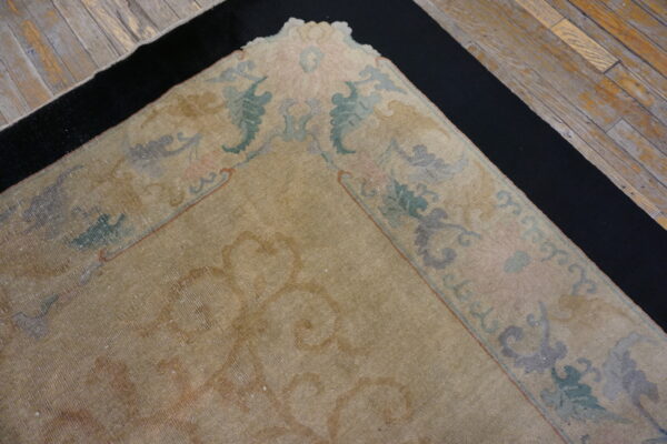 Faded tan rug with pastel floral border sits over a black mat on distressed wood floors.