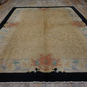 A large tan rug features tone-on-tone scrolling motifs bordered by pastel florals and a wide black edge on wood floors.