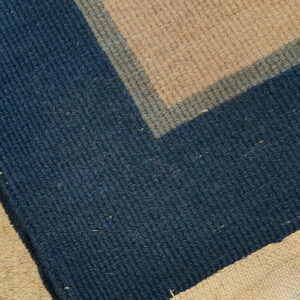 Geometric blue, sage, and tan striped rug corner with visible fringe, contrasting light shag texture.