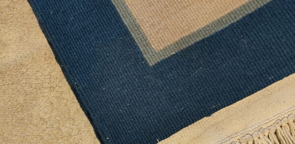 Minimalist vintage light blue and ivory white color open field chinese rug 3 Geometric blue, sage, and tan striped rug corner with visible fringe, contrasting light shag texture.