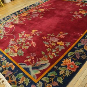 Plush red rug with intricate colorful floral patterns and a navy border on light plank wood flooring.