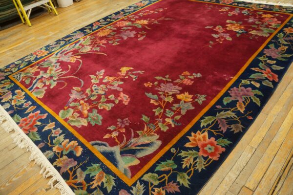 Plush red rug with intricate colorful floral patterns and a navy border on light plank wood flooring.
