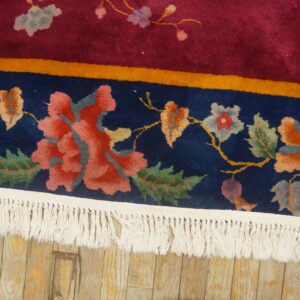 Detail of a high-pile floral rug featuring navy, magenta, and coral colors, with white fringe on a wood floor.