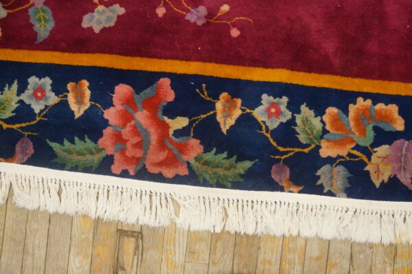 Detail of a high-pile floral rug featuring navy, magenta, and coral colors, with white fringe on a wood floor.