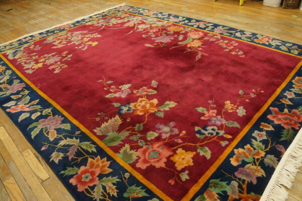 A deep red rug featuring a contrasting navy blue floral border is displayed on light hardwood floors.