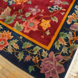 High-pile rug with red center and navy floral border accented by gold, visible on light wood flooring.
